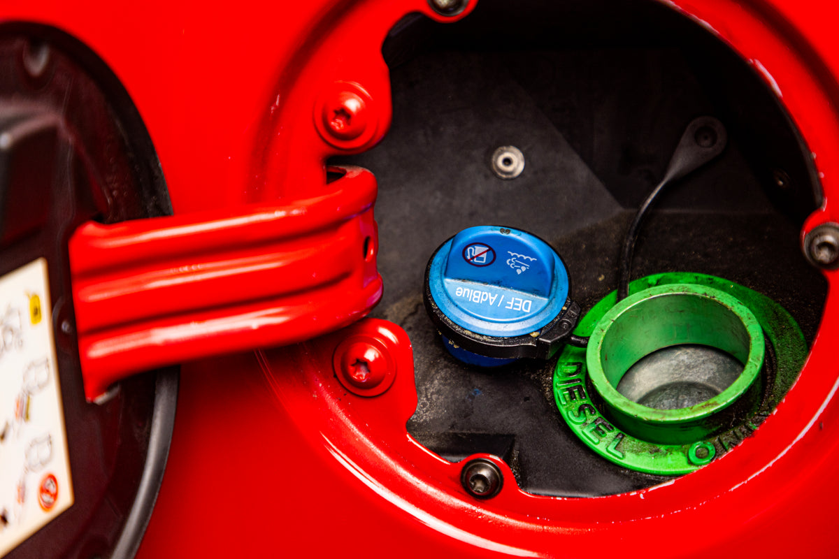 Blue DEF filler cap next to the diesel fuel filler on a red vehicle